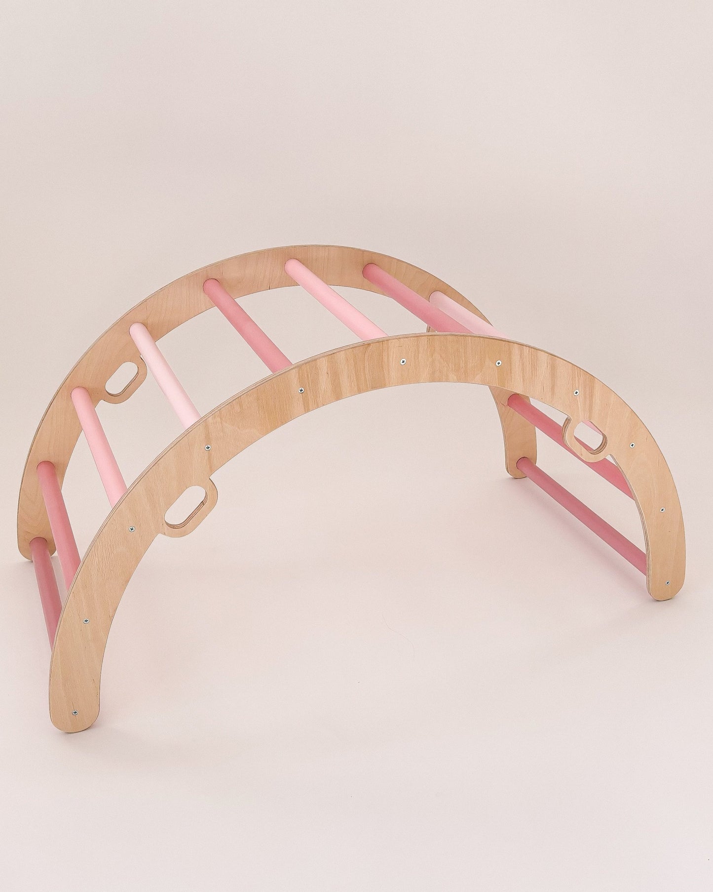 Criança a brincar com arco Pikler cor-de-rosa, desenvolvendo equilíbrio e coordenação.