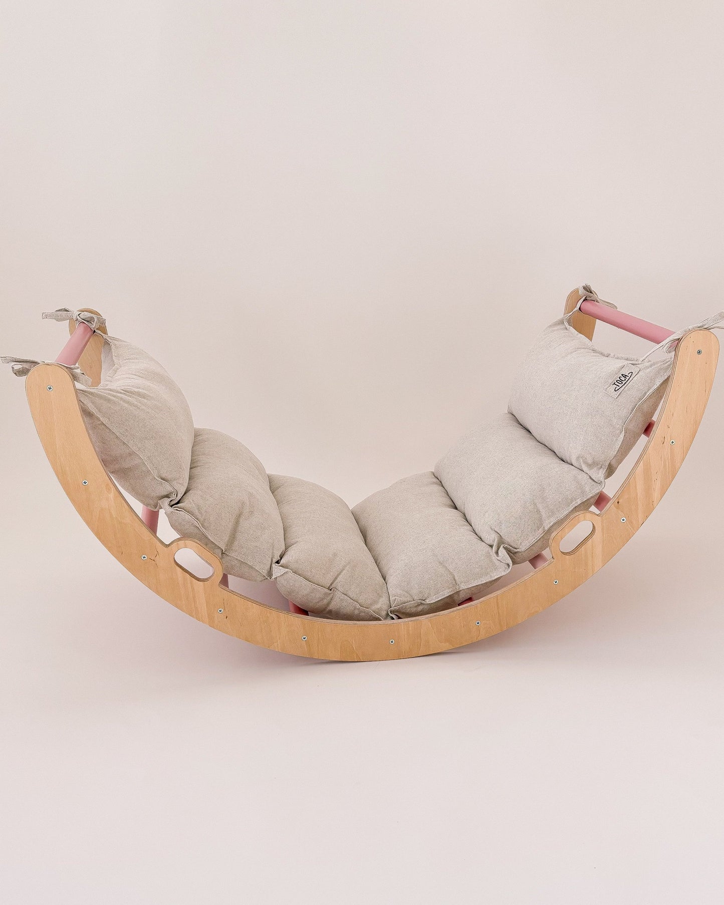 Criança a relaxar ou brincar no arco Pikler rosa com almofada, desenvolvendo equilíbrio e criatividade.