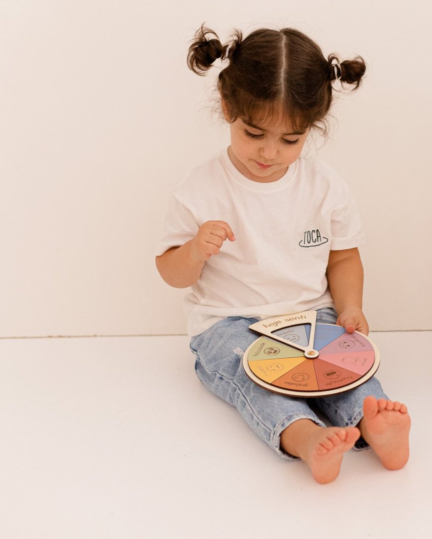 Menina de camisola branca e calças de ganga brinca com o quadro emoções.