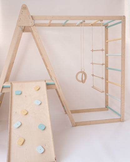 Parque infantil com estrutura de madeira, argolas e escadas suspensas para atividades motoras.