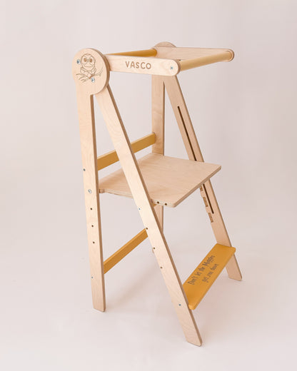 Torre de aprendizagem dobrável com estrutura em madeira, posicionada junto a uma bancada de cozinha.